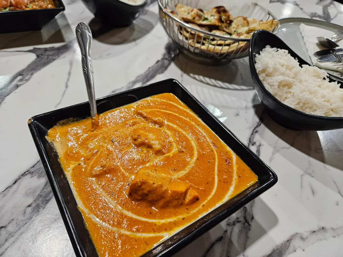 Butter chicken in a black bowl with garlic naan and basmati rice on a marble table