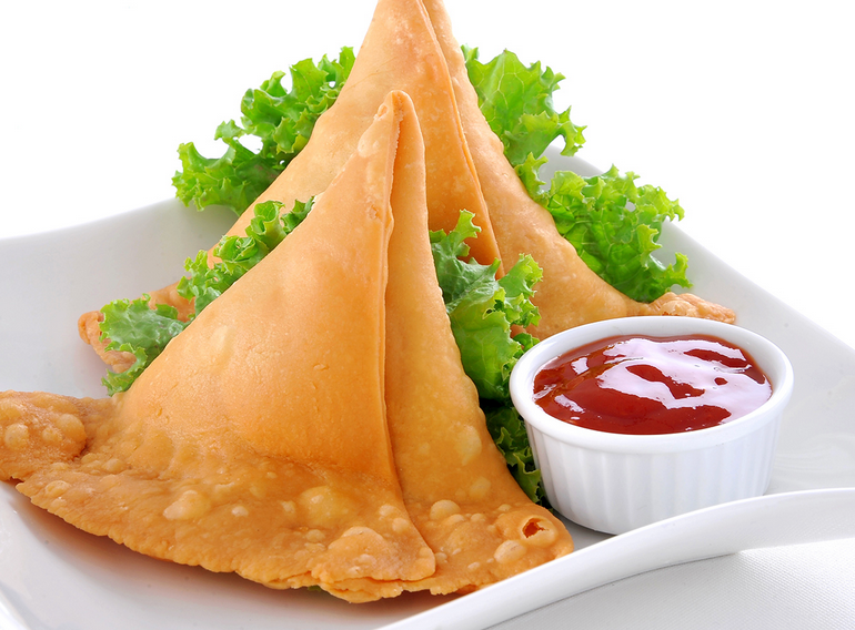 Vegetable samosas on a white plate with tamarind chutney and lettuce garnish
